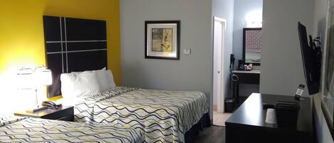 Habitación de hotel con cama, escritorio y silla. Hay un cuadro en la pared y una ventana.