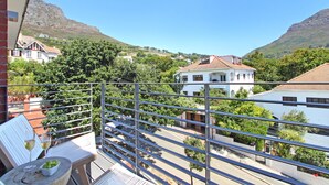 En balkon med udsigt over en by, et bord med en skål druer og glas, samt en stol.