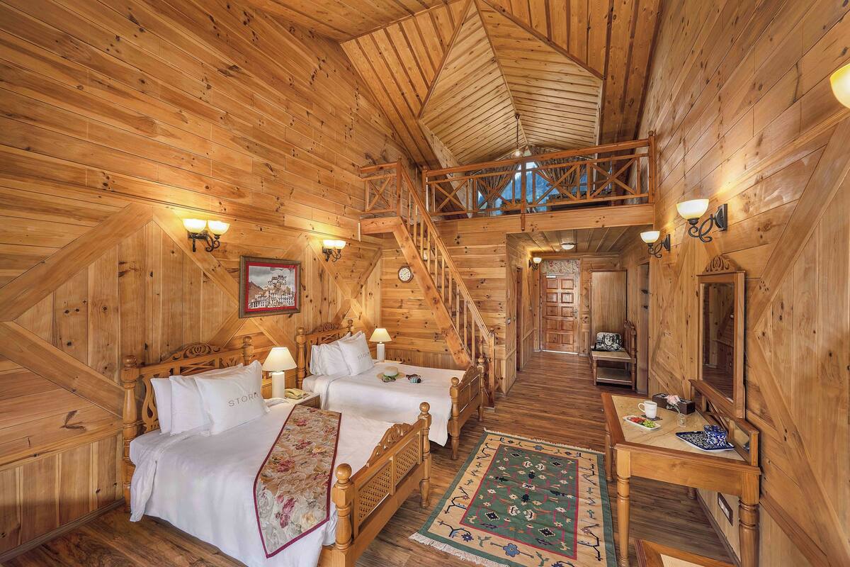 A wooden cabin with two bedrooms, a dining area, and a staircase connecting the floors.