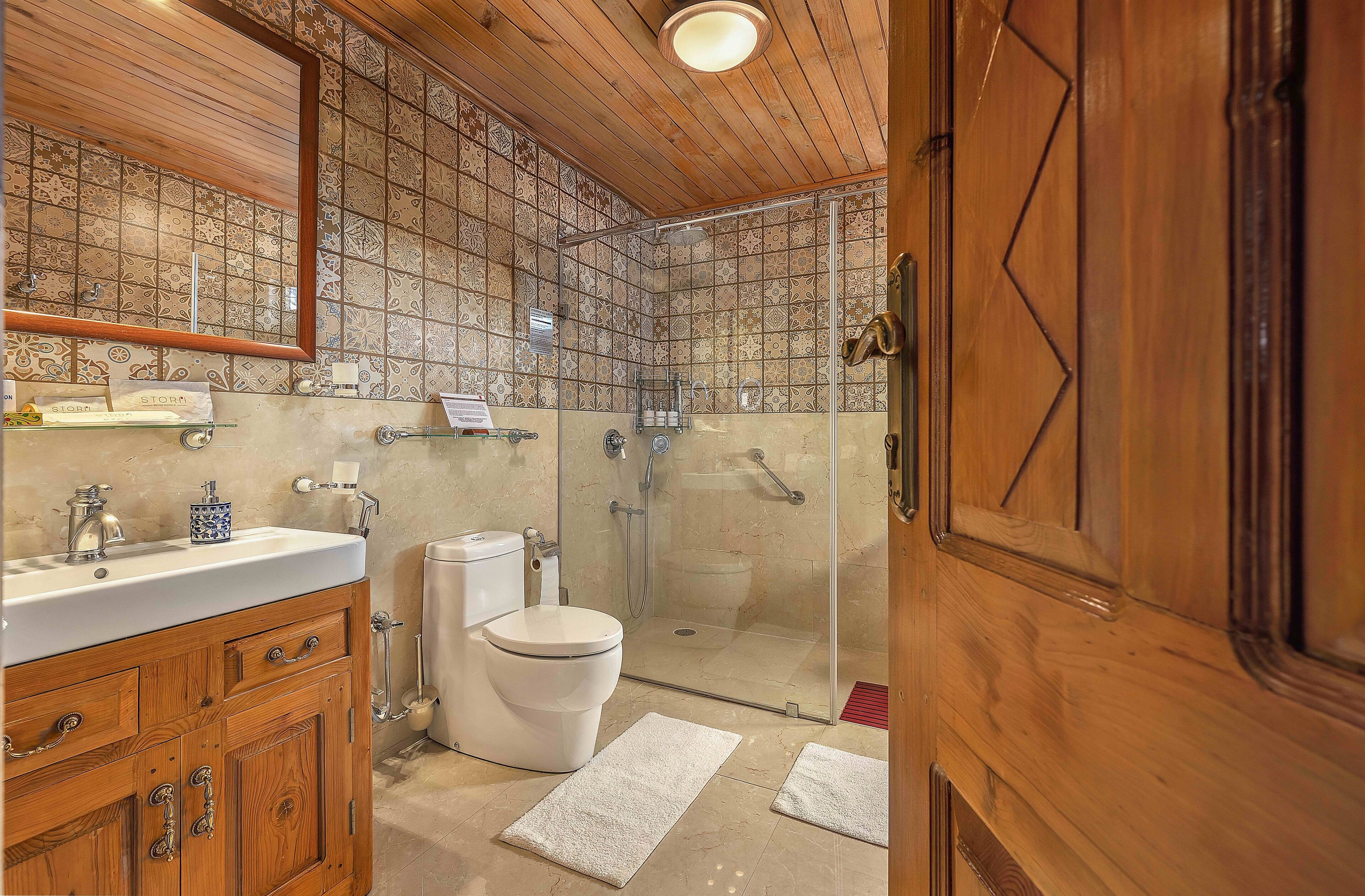 A bathroom with a wooden vanity, a toilet, a shower area with glass doors, and a tiled backsplash.