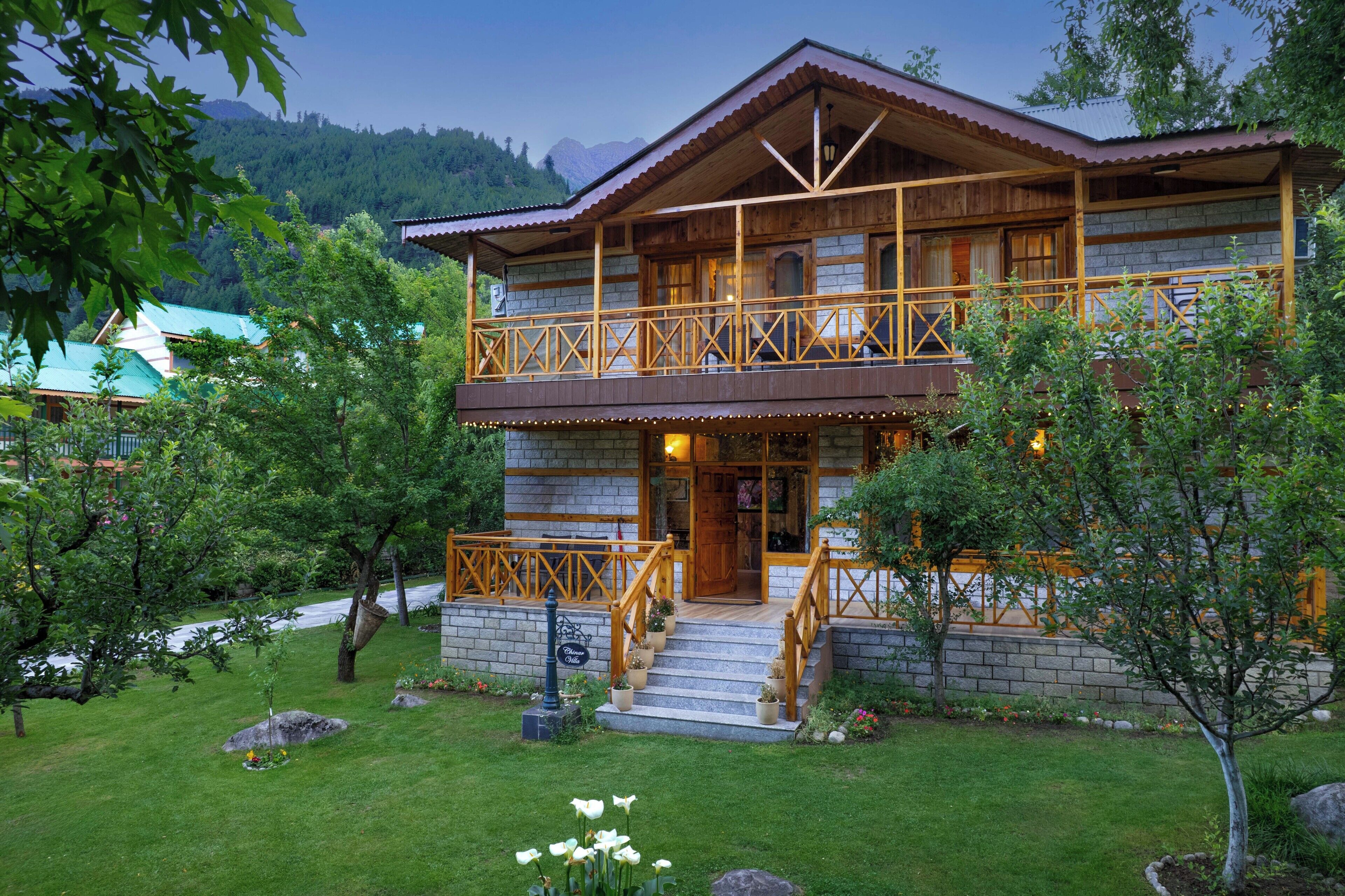A two-story wooden house with a balcony, surrounded by a well-maintained garden with rocks and plants.