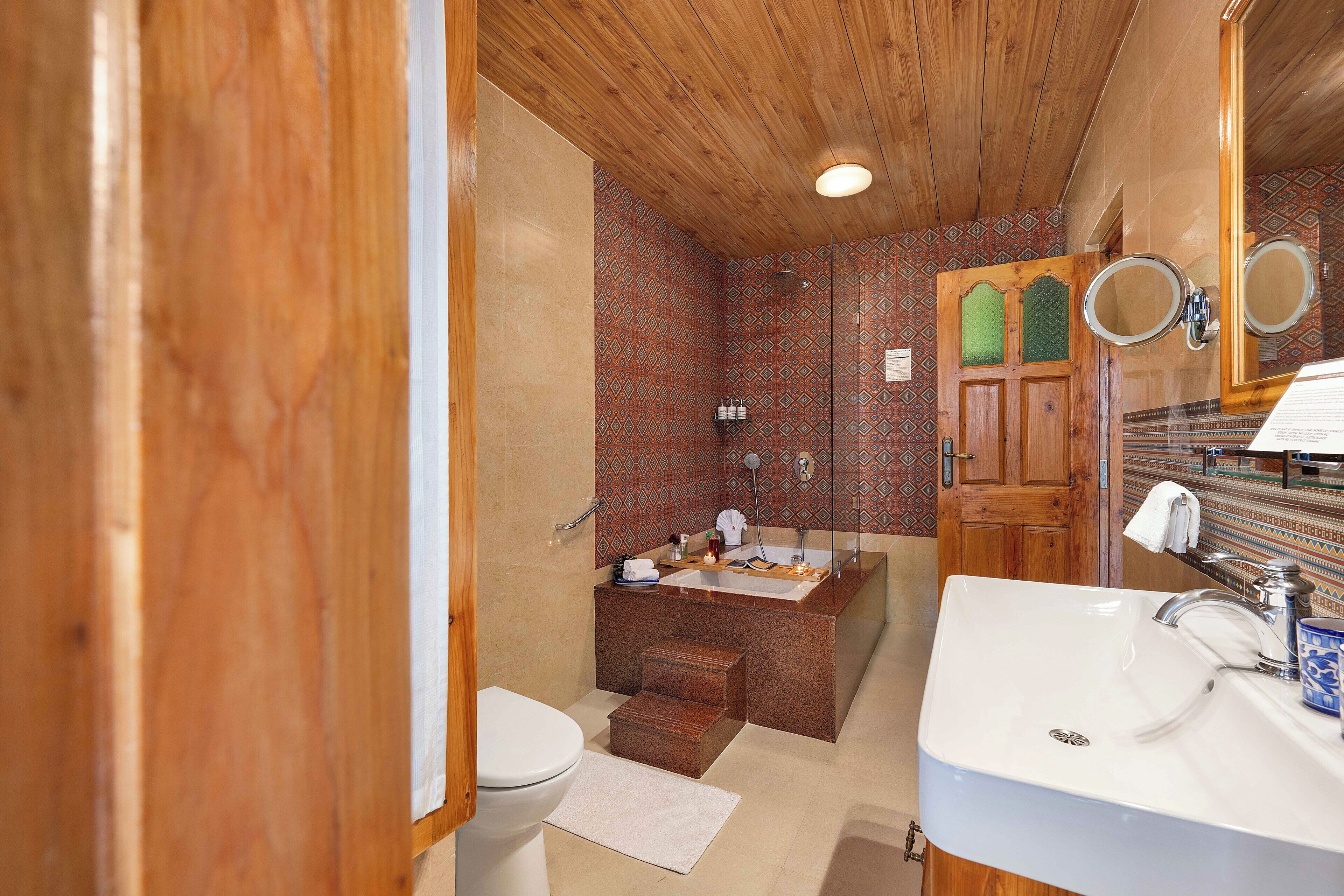 Baño con techo de madera, lavamanos blanco, bañera y zona de ducha.