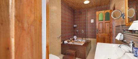 Baño con techo de madera, lavamanos blanco, bañera y zona de ducha.
