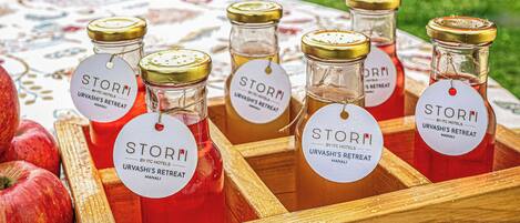 A wooden tray with several glass bottles labeled 'STORM URVASHI'S RETREAT MANALI' and a few apples.