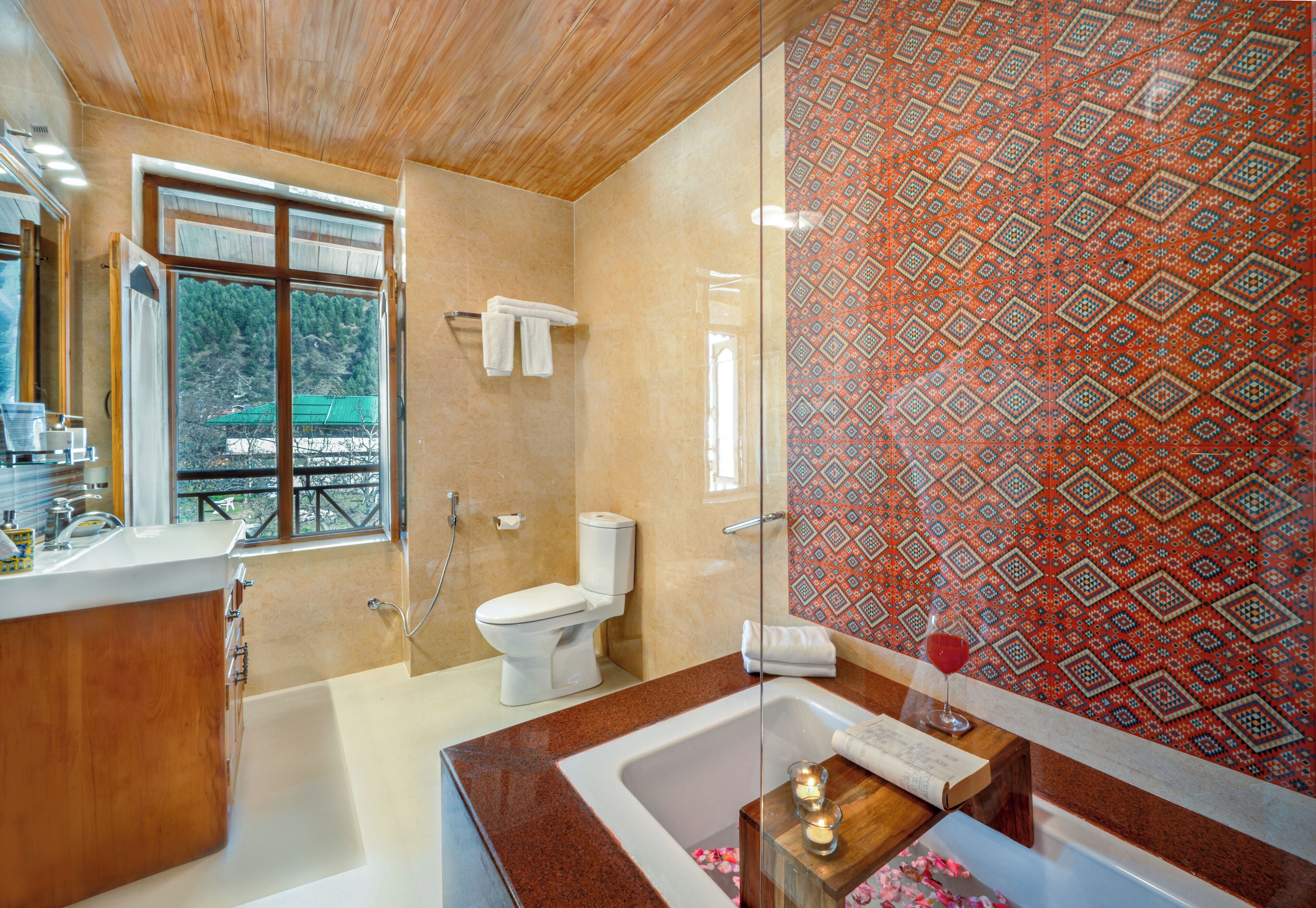 A modern bathroom with a wooden vanity, a large bathtub, and a patterned shower wall.
