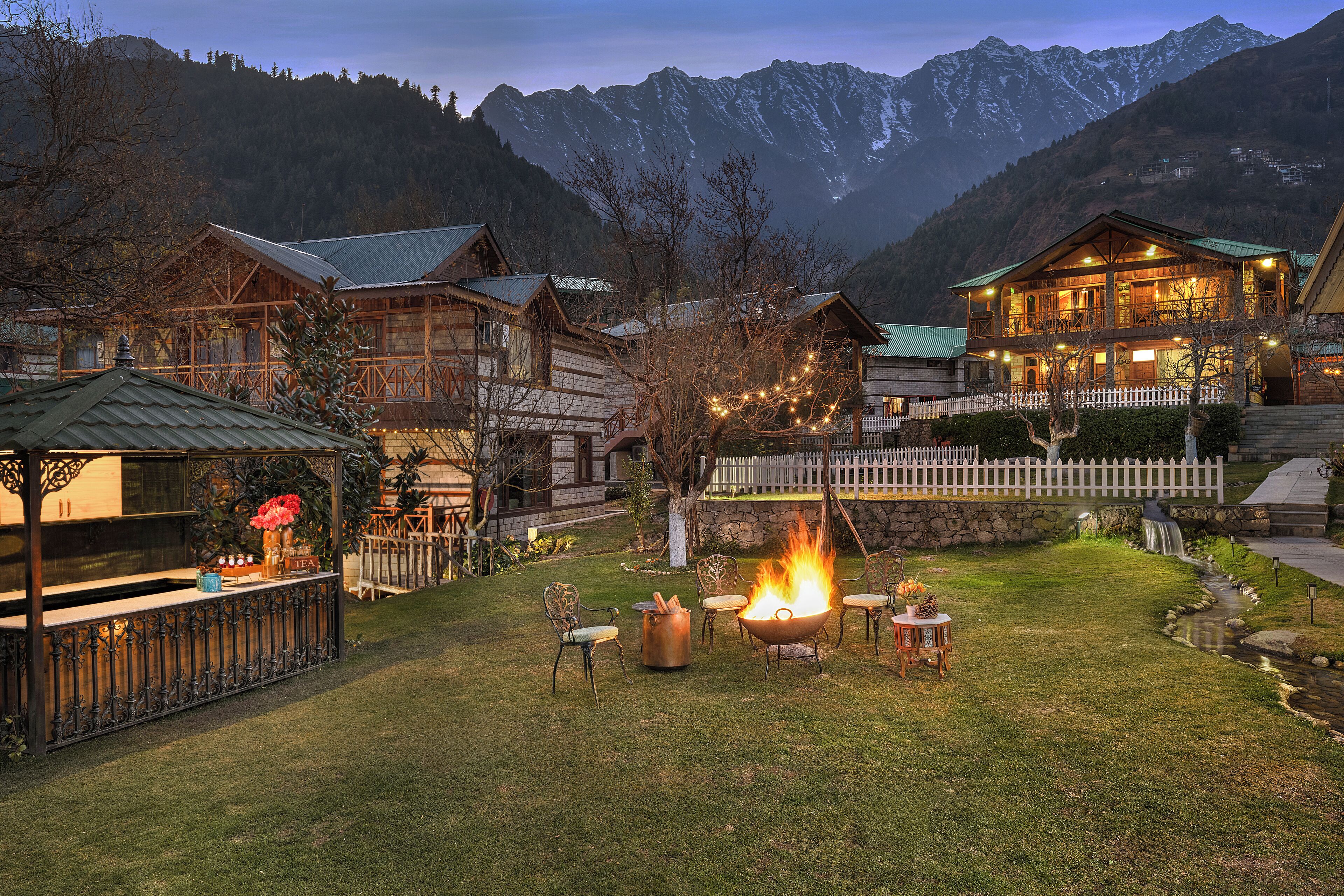 A rustic lodge with a fire pit and outdoor seating, surrounded by mountains.