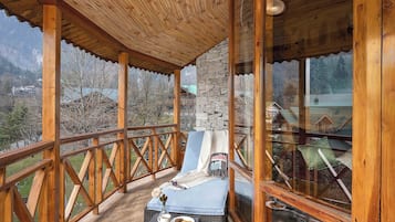 A wooden deck with a lounge chair and a small table, overlooking a mountainous landscape.