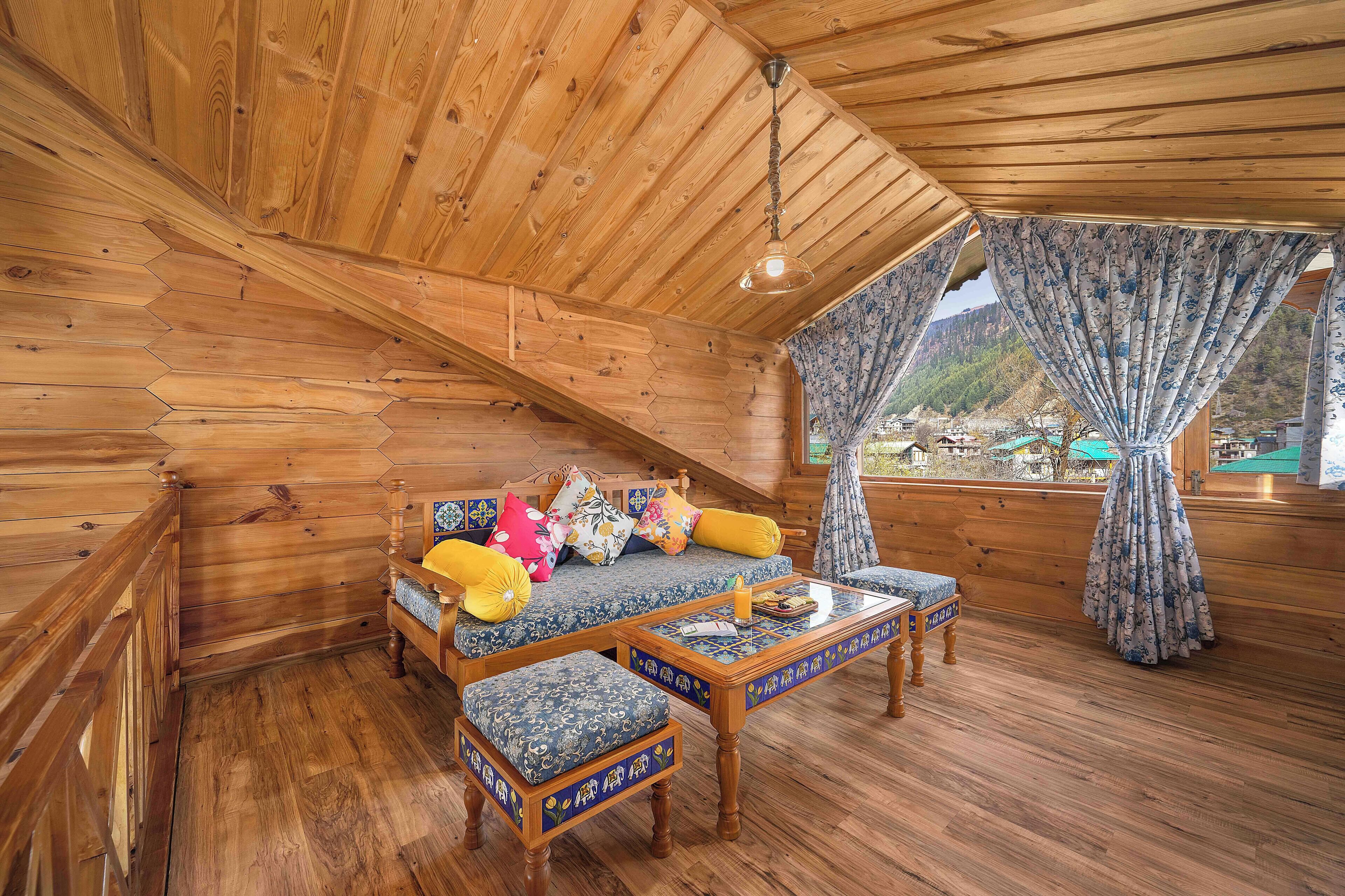 A wooden cabin interior with a sofa, two matching ottomans, a coffee table, and a window with curtains.