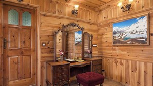 Una habitación de madera con suelo de madera, un aparador de madera con cajones, un espejo y un taburete tapizado en rojo.