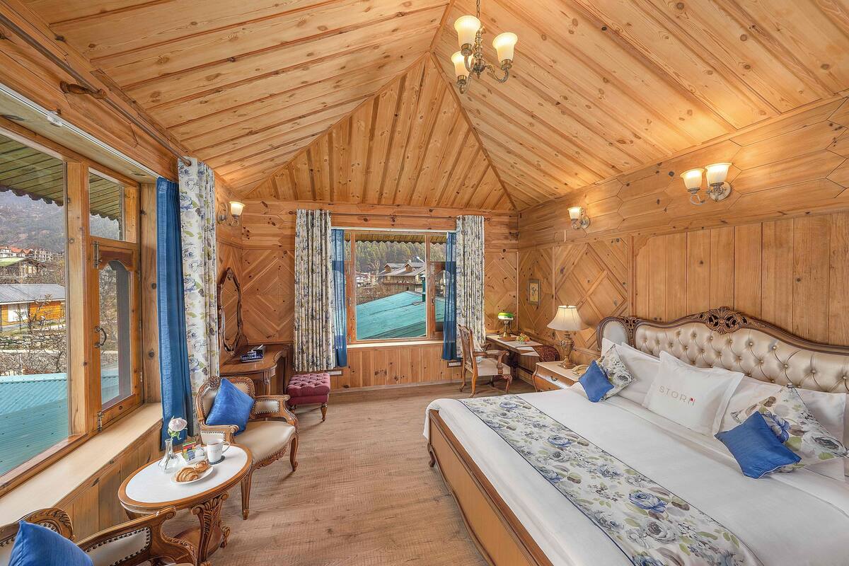 A wooden cabin room with a bed, a desk, and a view of a mountain.