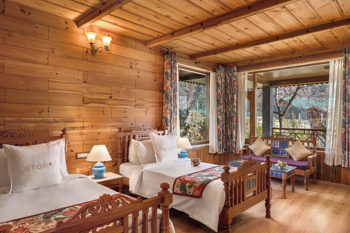A wooden cabin-style room with two beds, a small table, and a bench.