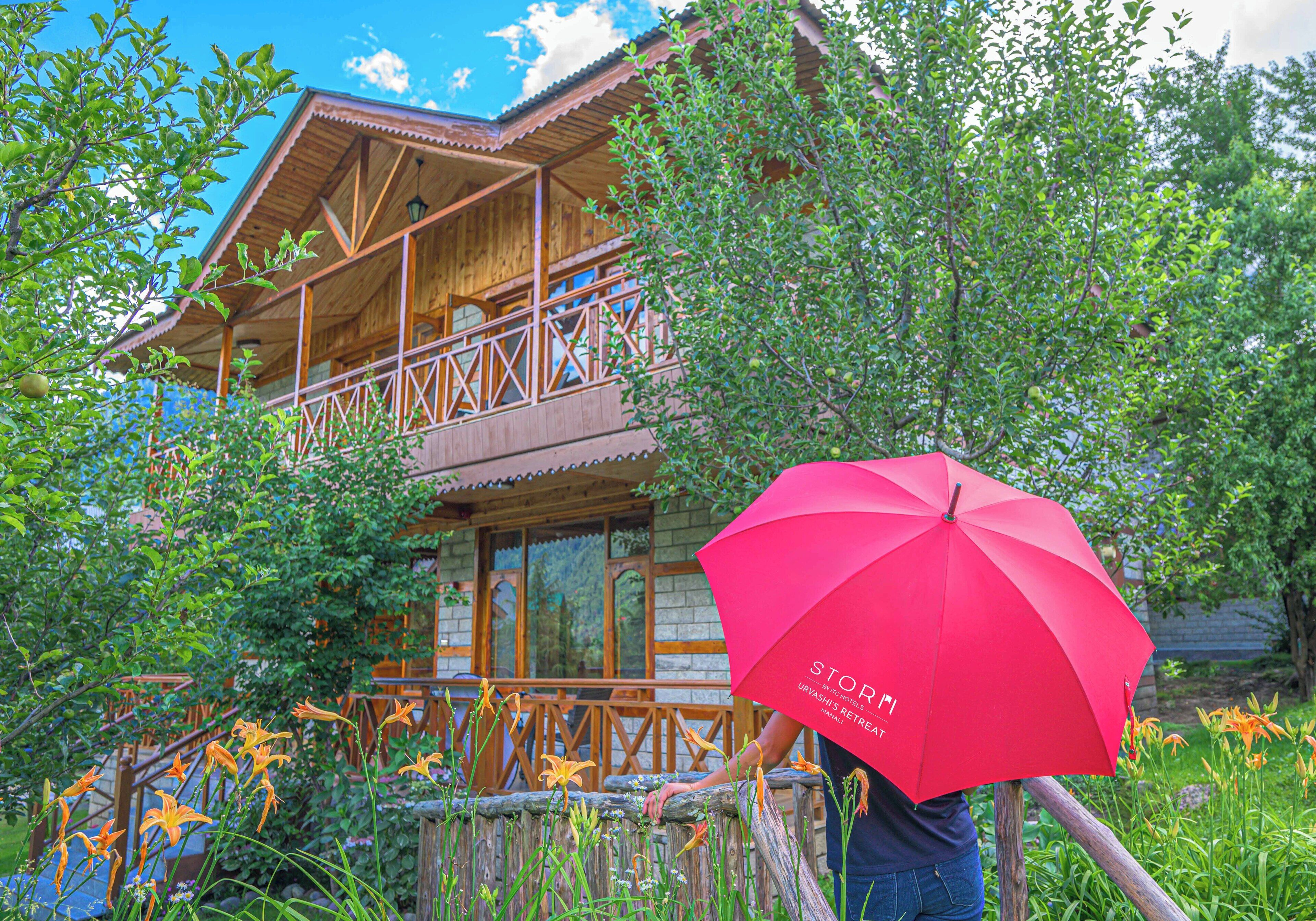 A wooden building with a balcony, surrounded by greenery and flowers.