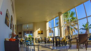 A spacious indoor area with large windows, tables, chairs, and artwork on the walls. - Akti Corali (Malevizi)