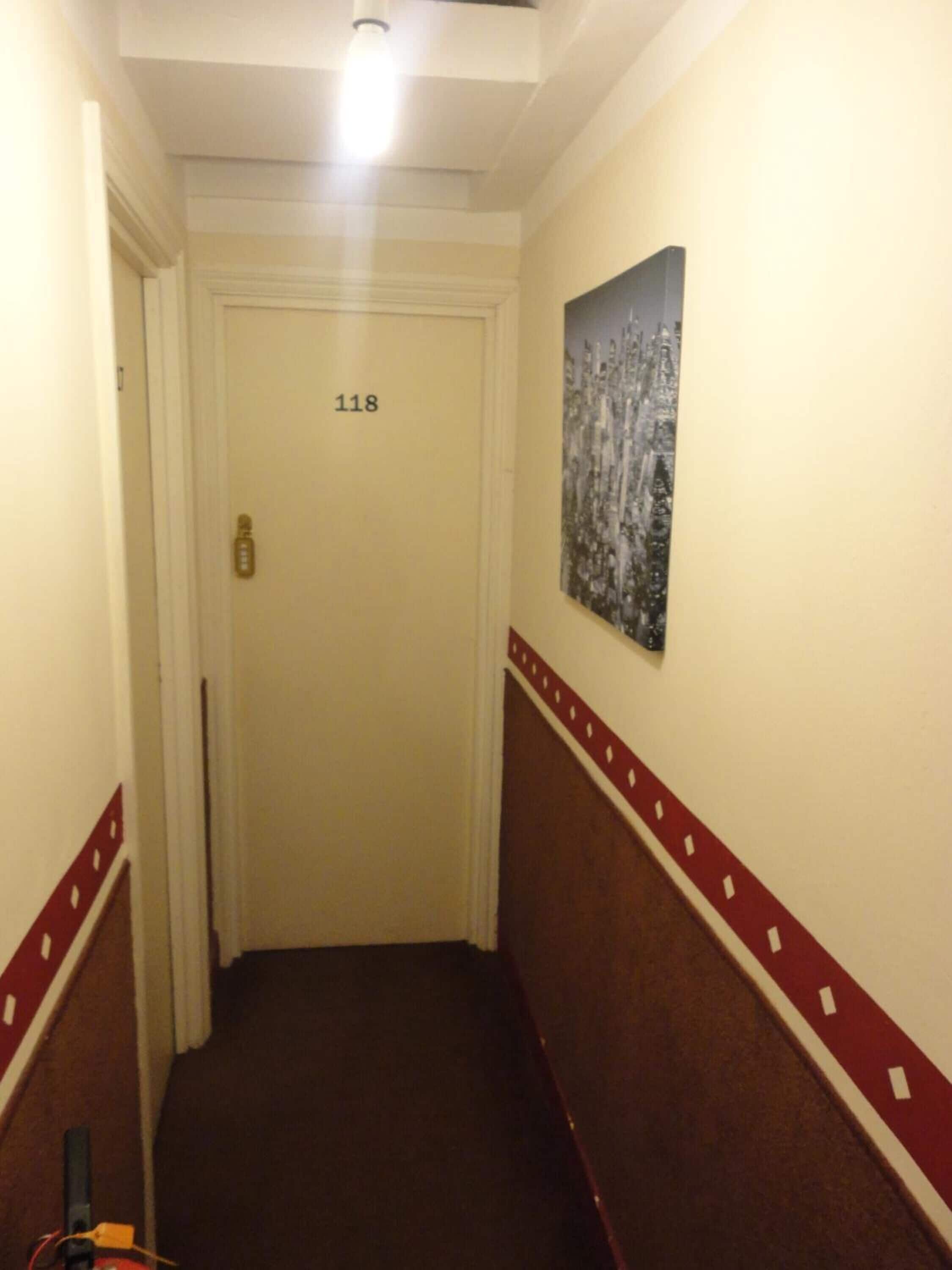 A narrow hallway with a door labeled "118", a red and white decorative border, and a winter-themed painting on the wall.