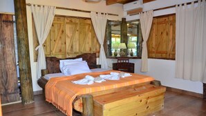 A wooden bed with a headboard, white bedding, and a wooden bench at the foot of the bed. - Kaz Ladouceur (La Digue)
