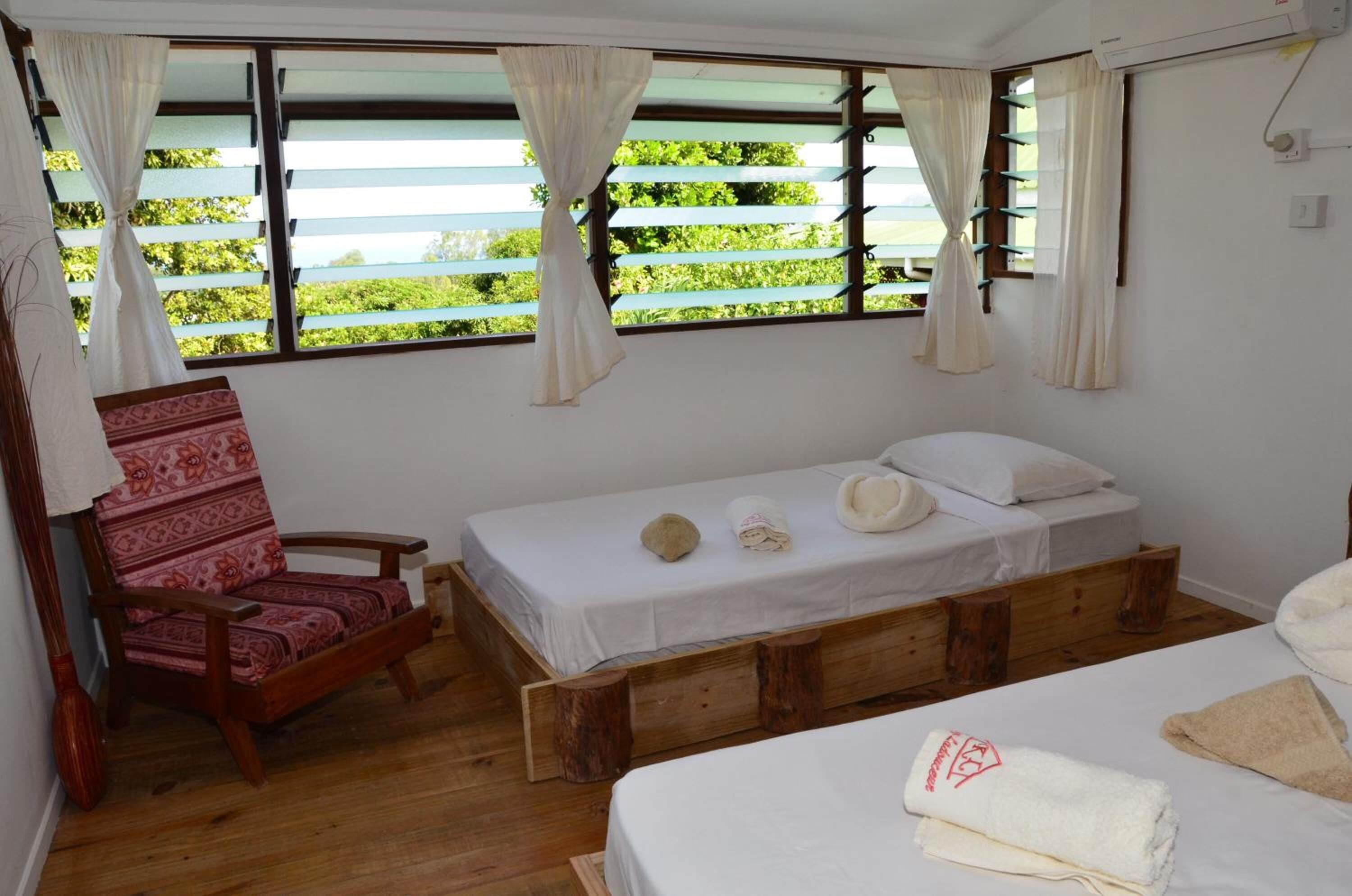 A room with a wooden bed, a patterned chair, and a window with curtains.