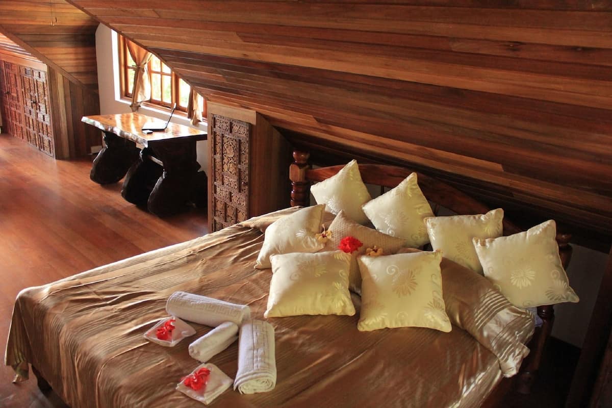 Ein Zimmer mit Holzboden, einem Bett, Kissen und einem Laptop auf einem Tisch.