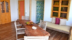 A wooden dining table with chairs, a bench with cushions, and a door with a leaf-patterned window. - Kaz Ladouceur (La Digue)