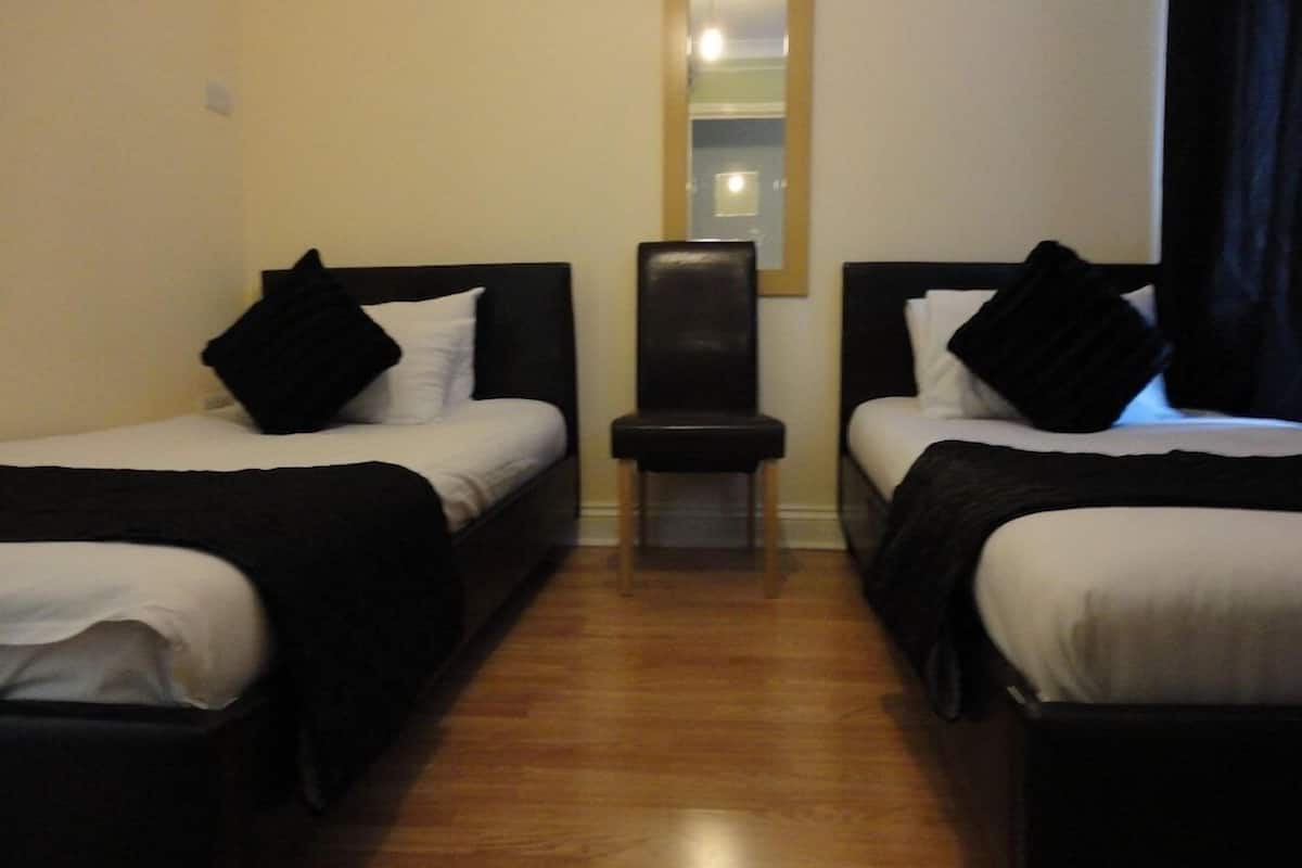 Una habitación con dos camas, un pequeño banco y un espejo en la pared.
