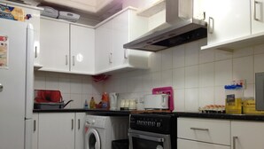 Cozinha compacta com armários brancos, máquina de lavar, torradeira e fogão.