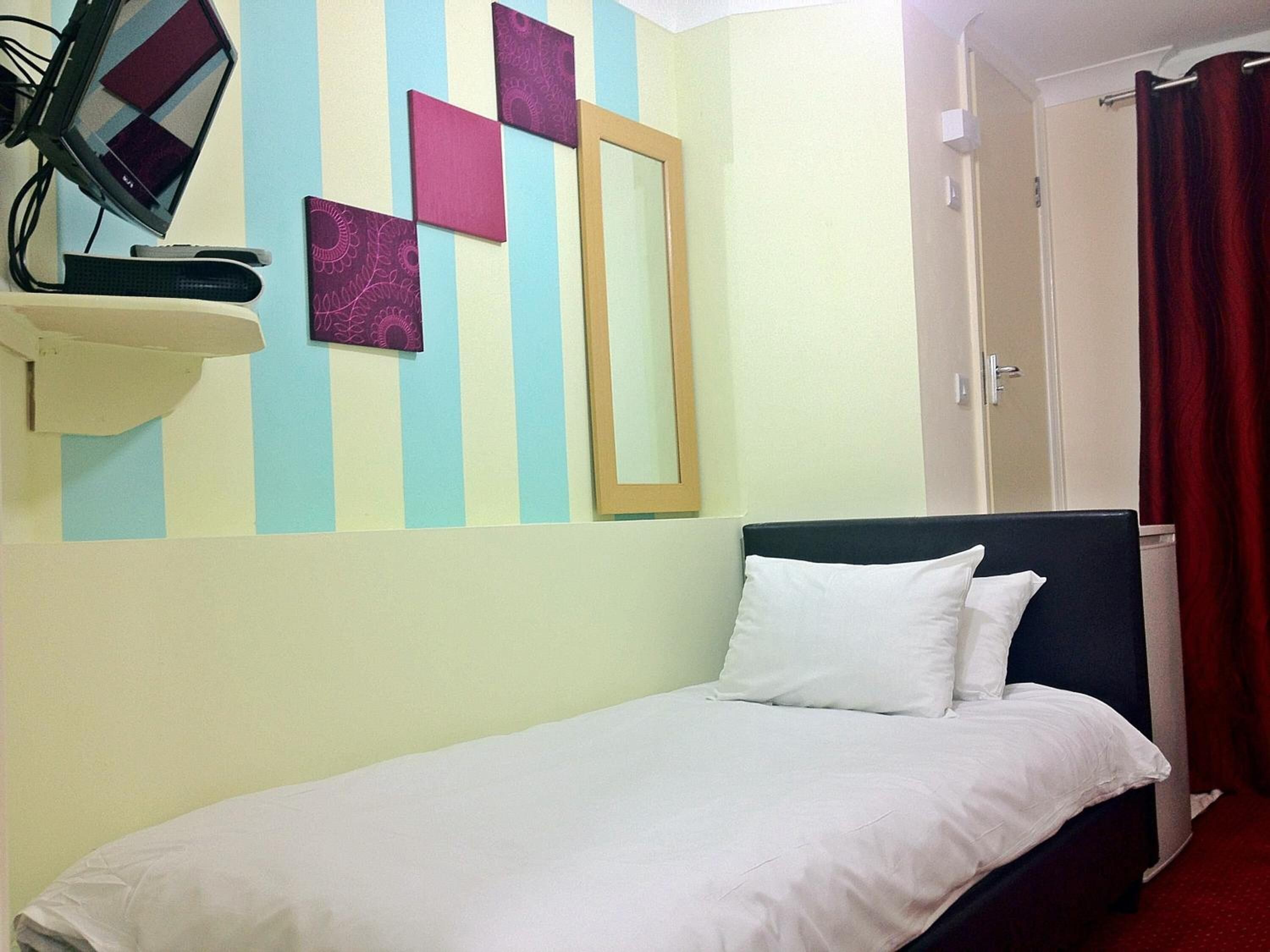 Cama bem arrumada com lençóis brancos em quarto com parede listrada, um espelho e uma televisão sobre um suporte.