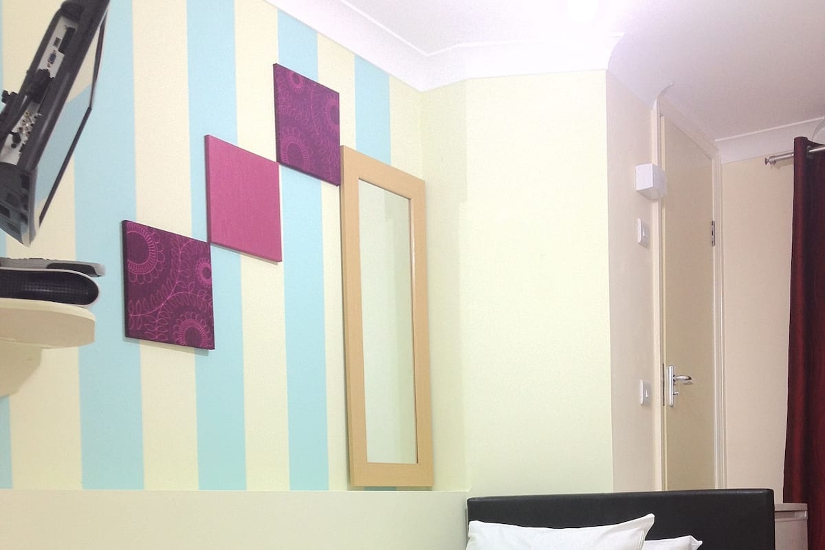 Una cama bien hecha con sábanas blancas en una habitación con paredes a rayas, un espejo y una puerta.