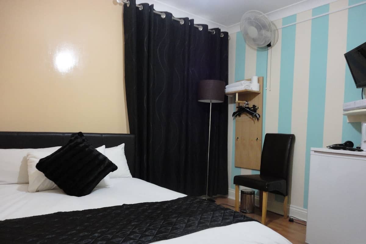 Una habitación de hotel con cama, escritorio, silla, ventilador y armario.
