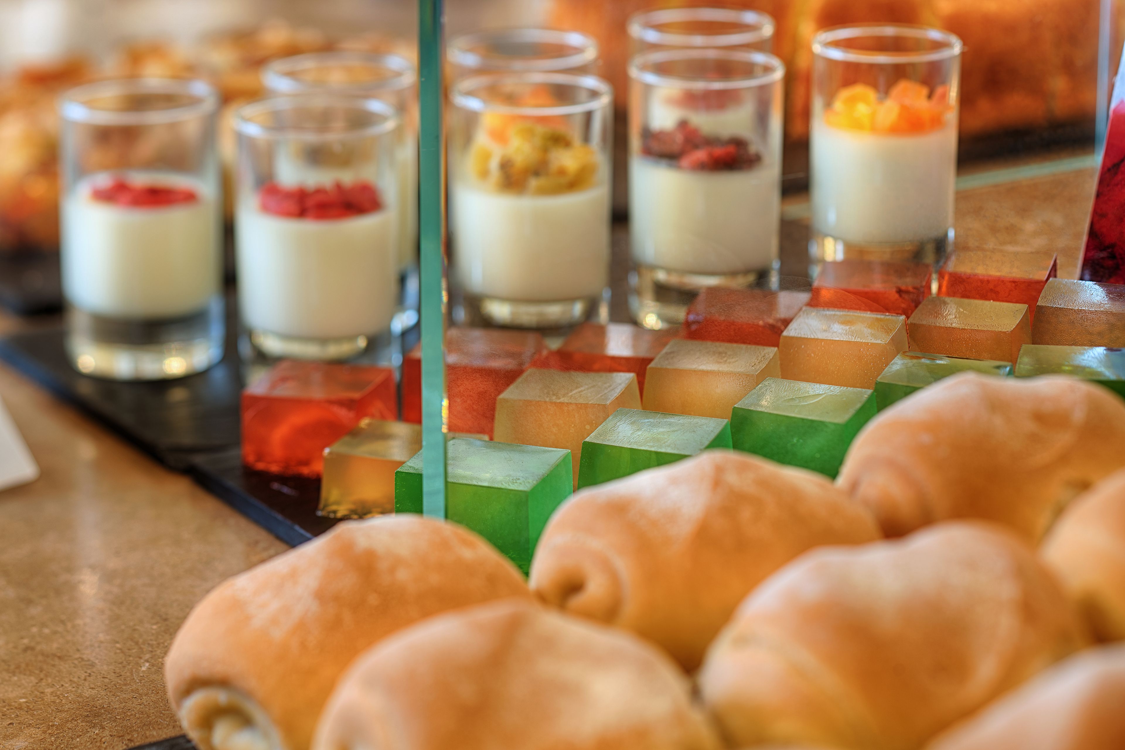 Un présentoir de desserts proposant une variété de douceurs, notamment de petits verrines de desserts en couches et des cubes de gelée de couleurs vives.