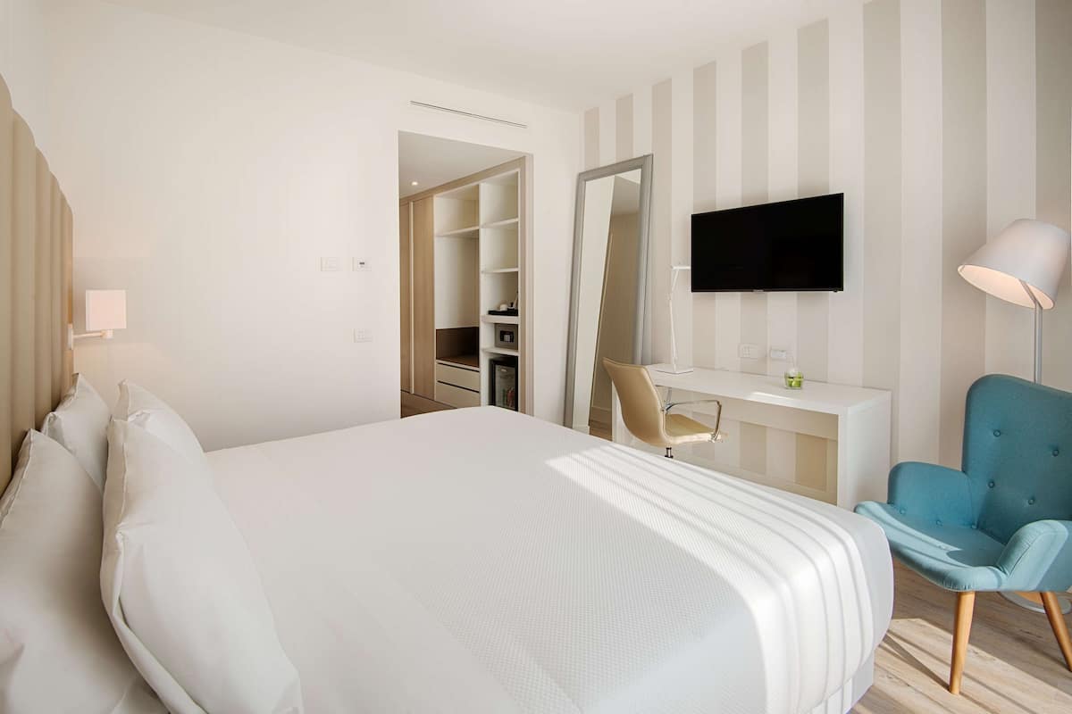 A hotel room with a bed, a desk, a chair, a TV, and a wardrobe.