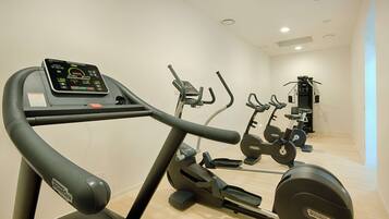 A gym with a treadmill, elliptical, and stationary bike, featuring a control panel and a light wooden floor.