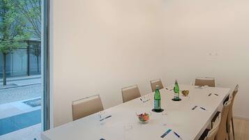 A conference room with a long table, chairs, and a window with a view of trees and a building.