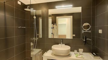 A modern bathroom with a glass-enclosed shower, a round mirror, and a white sink with toiletries.