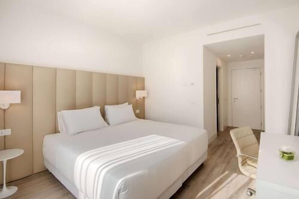 A hotel room with a large bed, bedside lamps, a chair, and a desk.