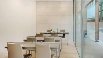 Un salón de conferencias con varias mesas y sillas, ventanas amplias y vistas al exterior.