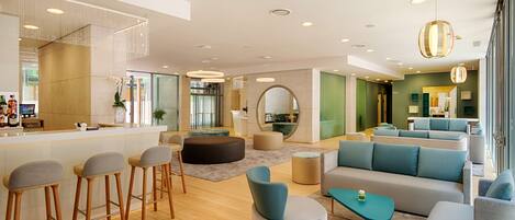 A modern hotel lobby with a bar area, seating arrangements, and a large mirror.