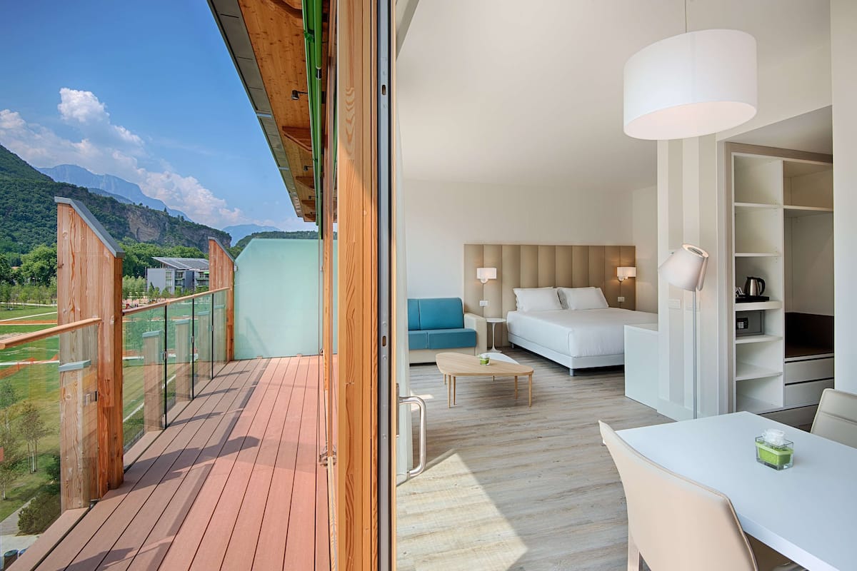 A modern hotel room with a balcony, a bed, a sofa, a table, and a walk-in closet.