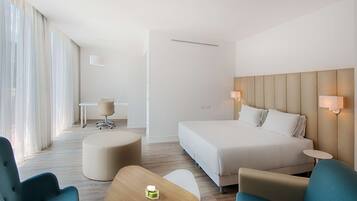 Una habitación de hotel moderna con una cama grande, dos sillones, una mesita y un escritorio con silla.
