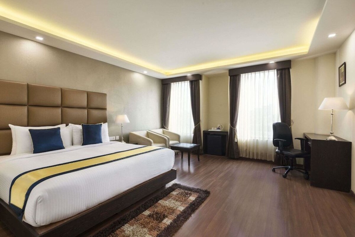 A hotel room with a large bed, a desk, a chair, and a sofa.