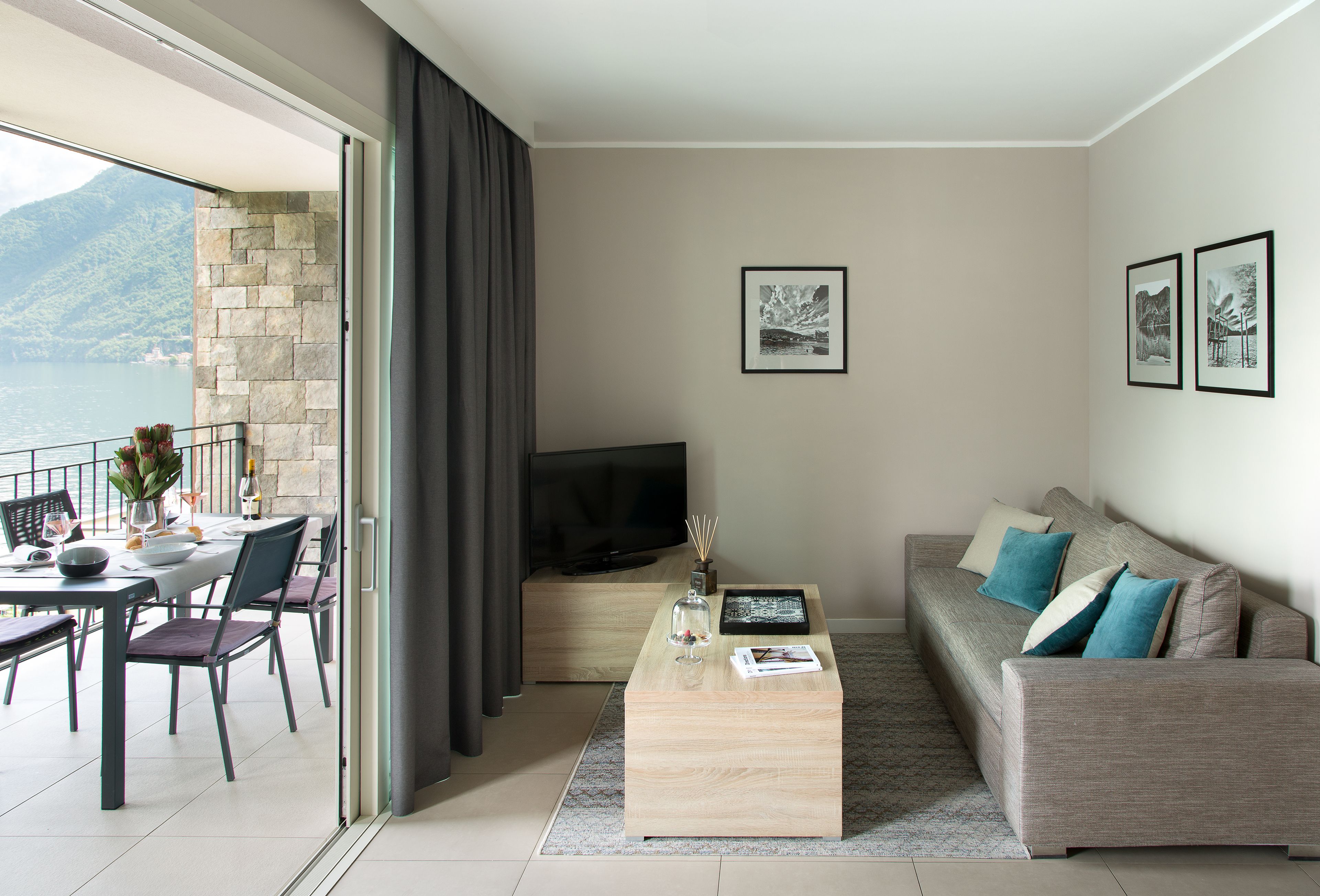 Un salon moderne avec un canapé, une table basse et un téléviseur. On aperçoit un balcon d’où l’on a une vue sur les montagnes.