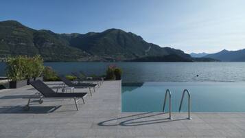Uma área de piscina com espreguiçadeiras e vista para um lago e montanhas.