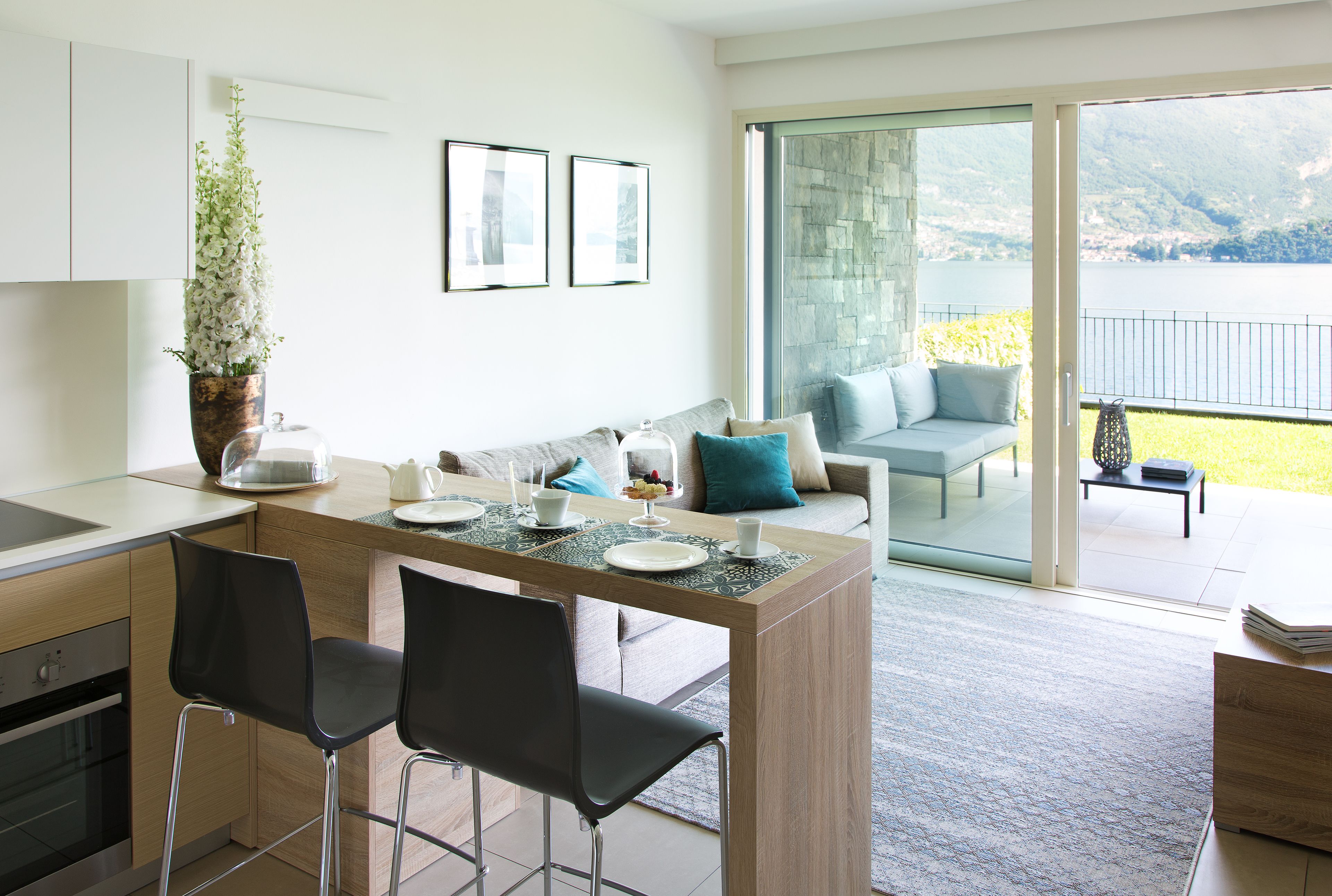 A modern kitchen with a dining area, a large window with a view of mountains, and a balcony with a sofa.