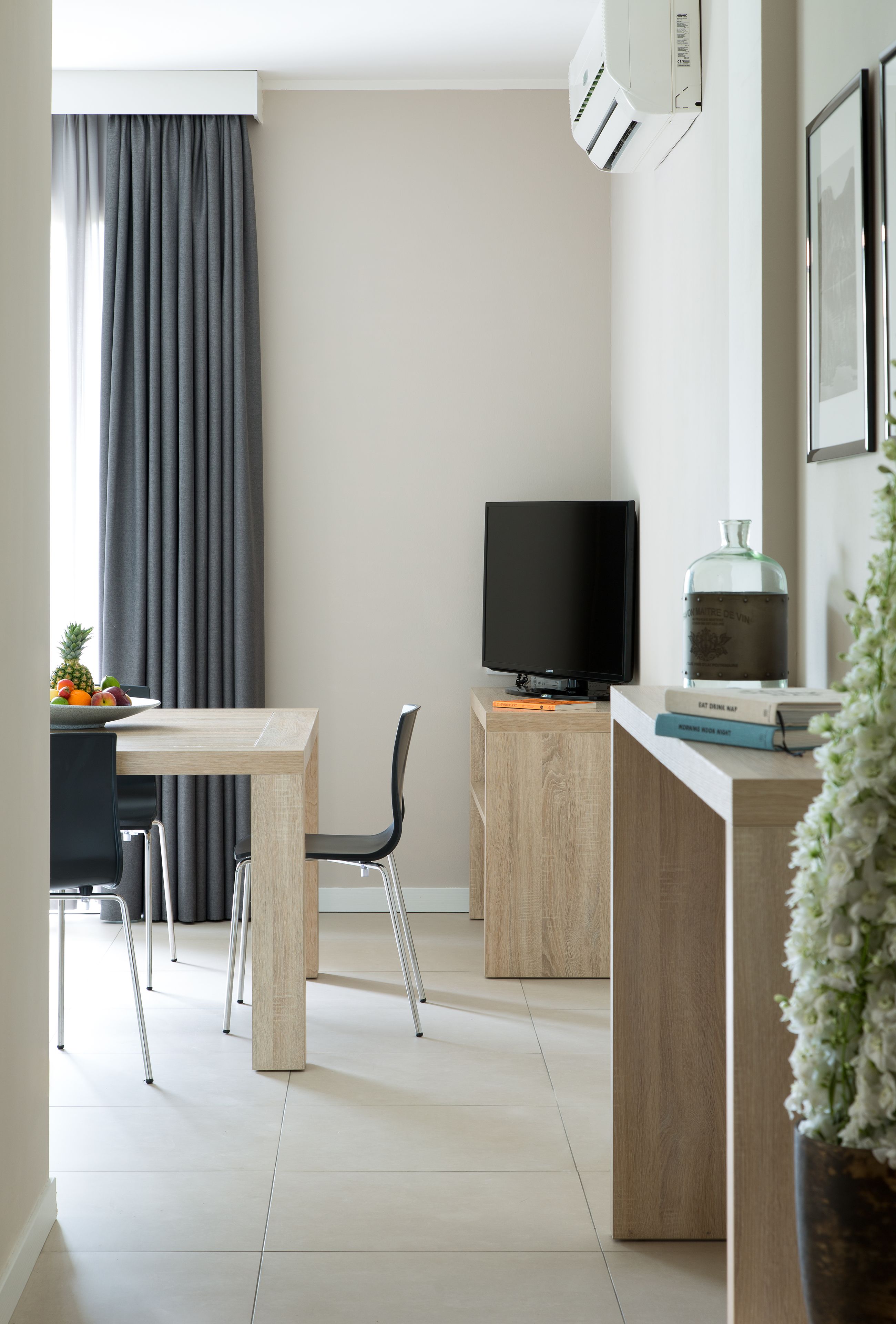 A modern kitchen with a dining table, chairs, a TV, and a small plant.
