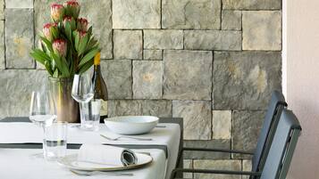 Mesa servida con un jarrón de flores, copas de vino y platos, con un fondo de pared de piedra.