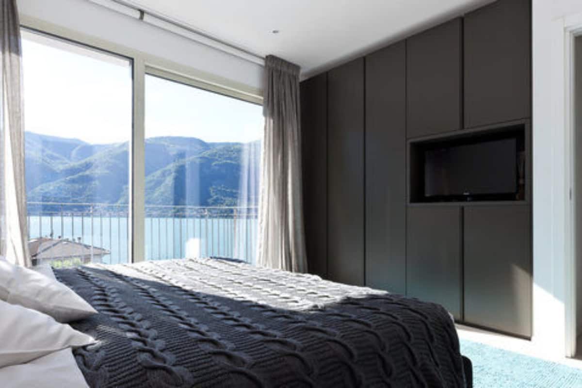 Een slaapkamer met een groot bed, een aan de muur bevestigde televisie en uitzicht op bergen door grote ramen.