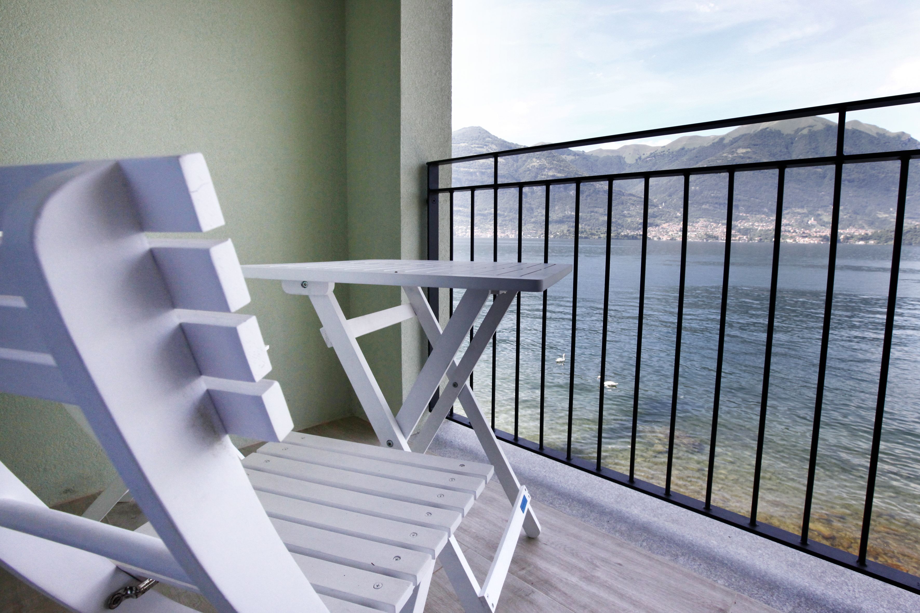 Une chaise blanche sur un balcon, avec vue sur un lac et des montagnes.