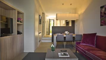 A modern living room with a flat-screen TV, a coffee table with a magazine, a red sofa, and a dining area with chairs and a table.