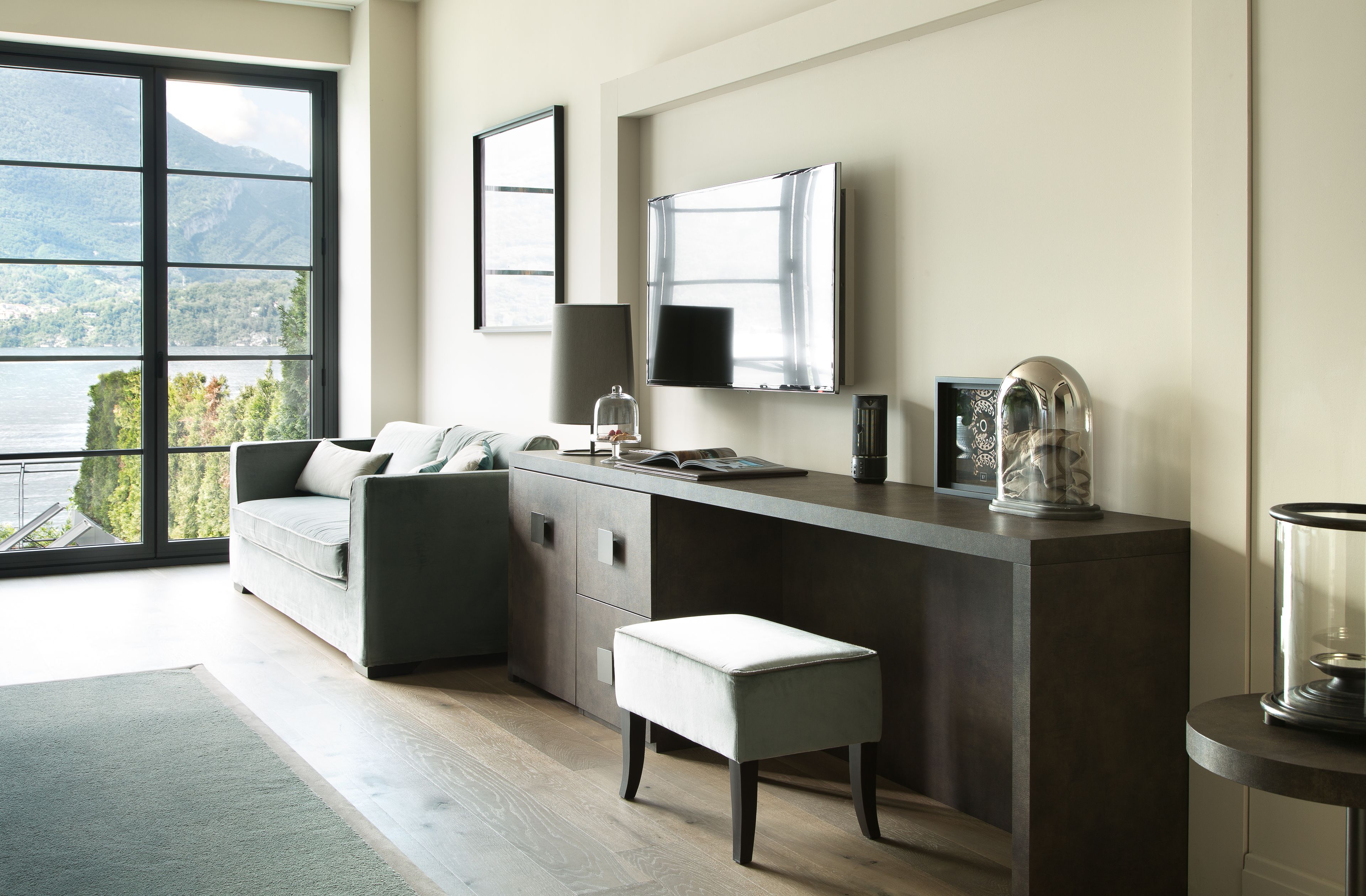A modern room with a large window, a sofa, a desk, and a view of mountains.