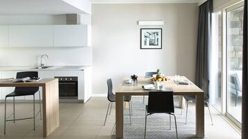 Una cocina moderna con armarios blancos, un comedor con mesa y sillas de madera, y un ventanal con cortinas.