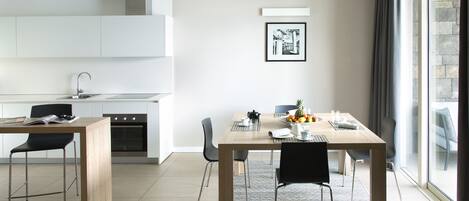 A modern kitchen with white cabinets, a dining area with a wooden table and chairs, and a large window with curtains.