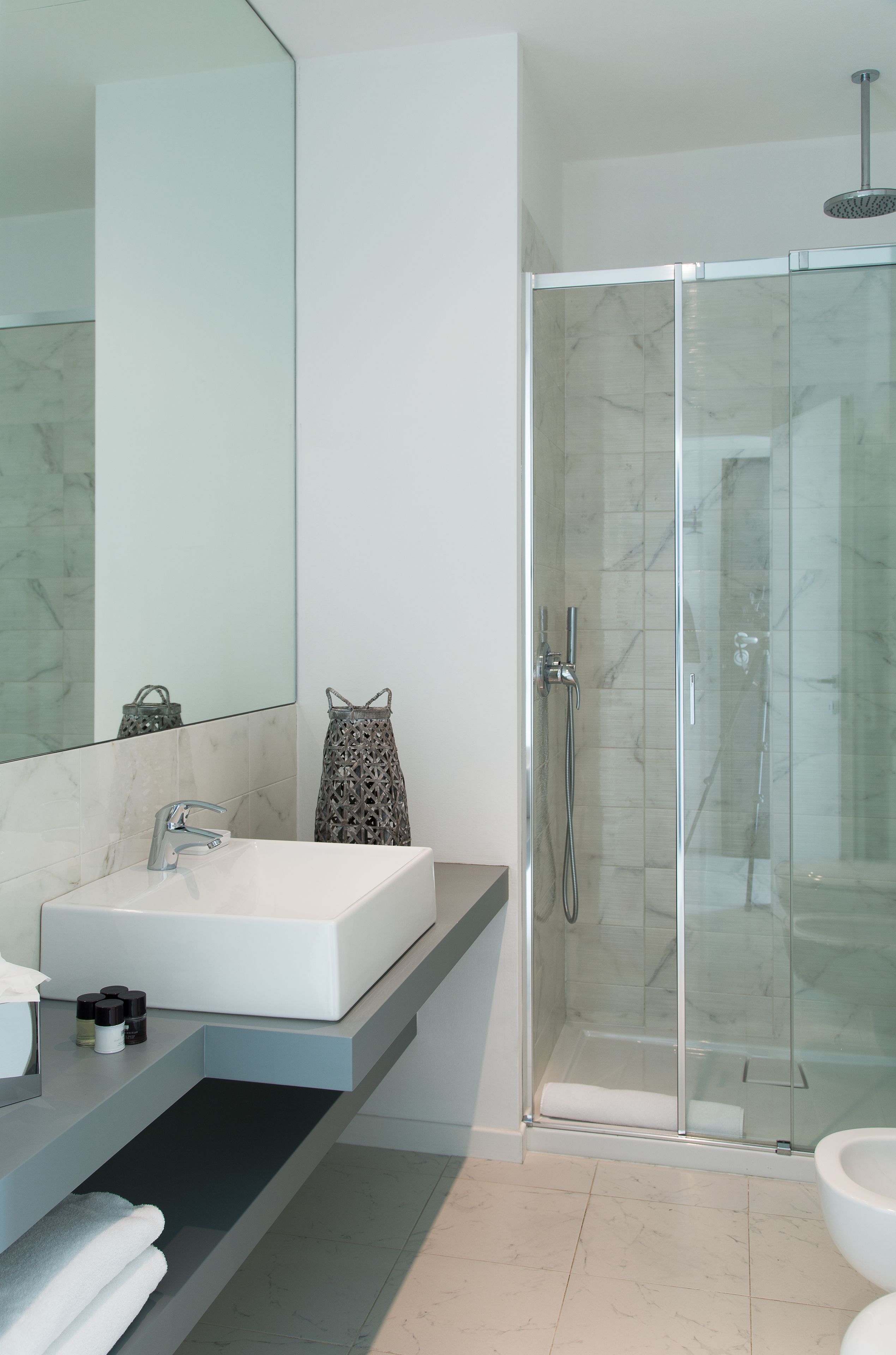 Une salle de bain moderne avec un lavabo blanc, un grand miroir, une douche en verre et un porte-serviettes.